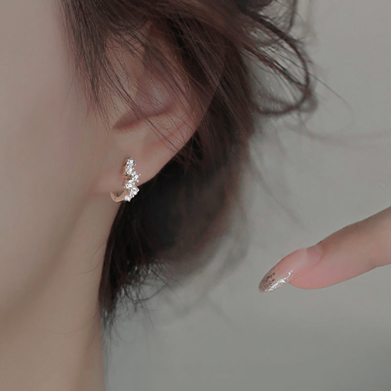 Silver hoop earring on earlobe, encrusted with sparkling clear crystals in an asymmetrical cluster design.