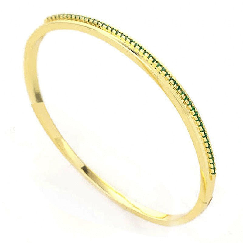 Gold metal hinged bangle bracelet featuring a row of pave-set green crystals along the outer edge.