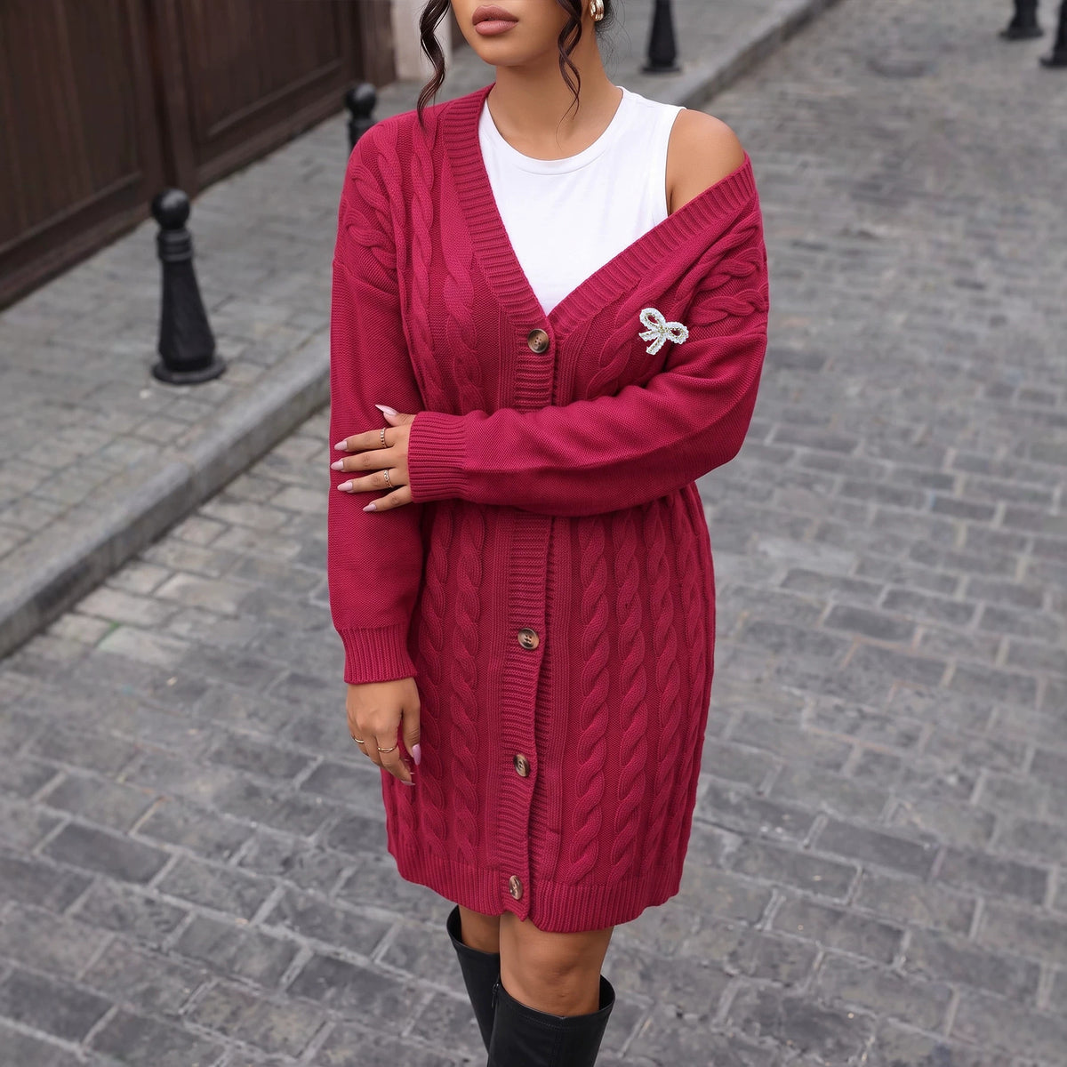 A long sleeve, cable-knit maroon cardigan with brown buttons is worn open over a white top.