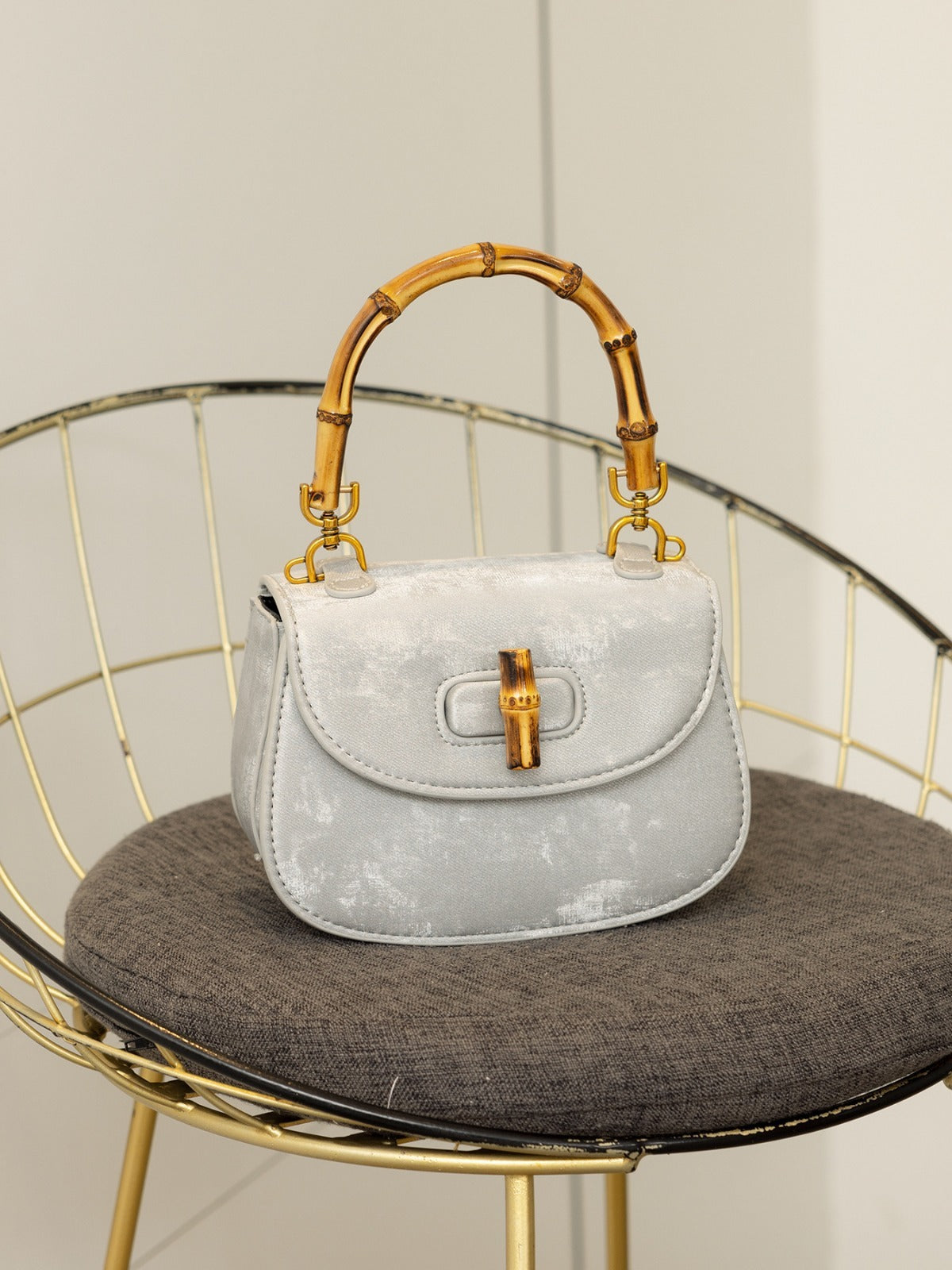 Light grey marbled-fabric handbag with bamboo top handle and bamboo turn-lock clasp on a chair.