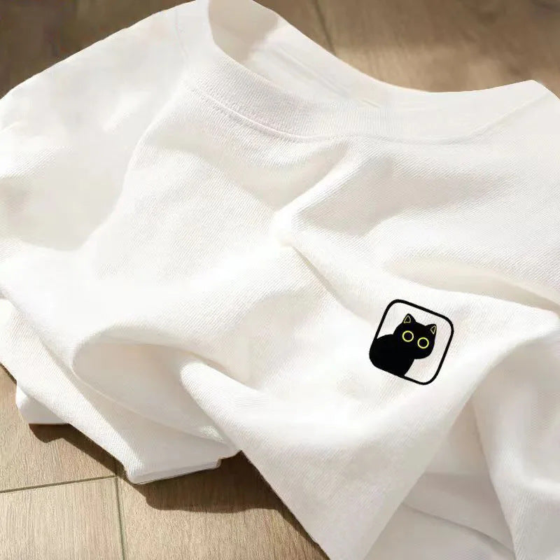 A folded white crewneck t-shirt with a small black cat patch featuring yellow eyes.