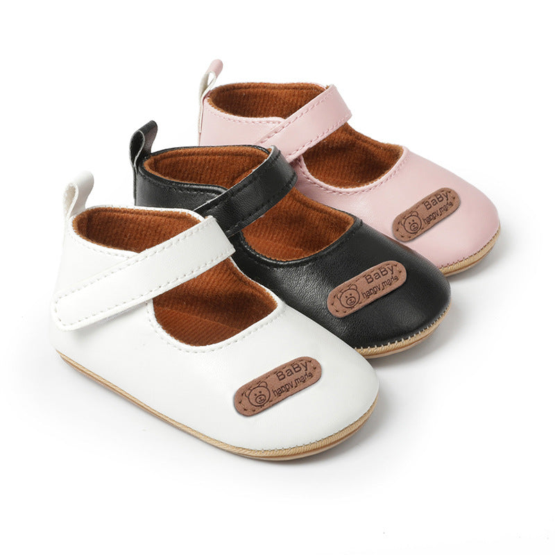 Three baby Mary Jane shoes in white, black, and pink leather with hook-and-loop straps and a teddy bear patch.