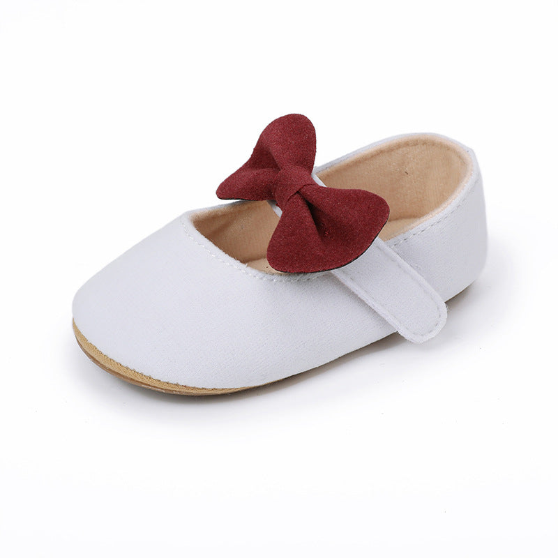 White infant Mary Jane shoe with a red bow and velcro strap.