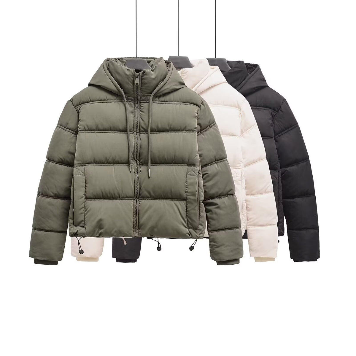 Three hooded puffer jackets hanging on hangers in olive green, cream, and black with zippered fronts and drawstrings.