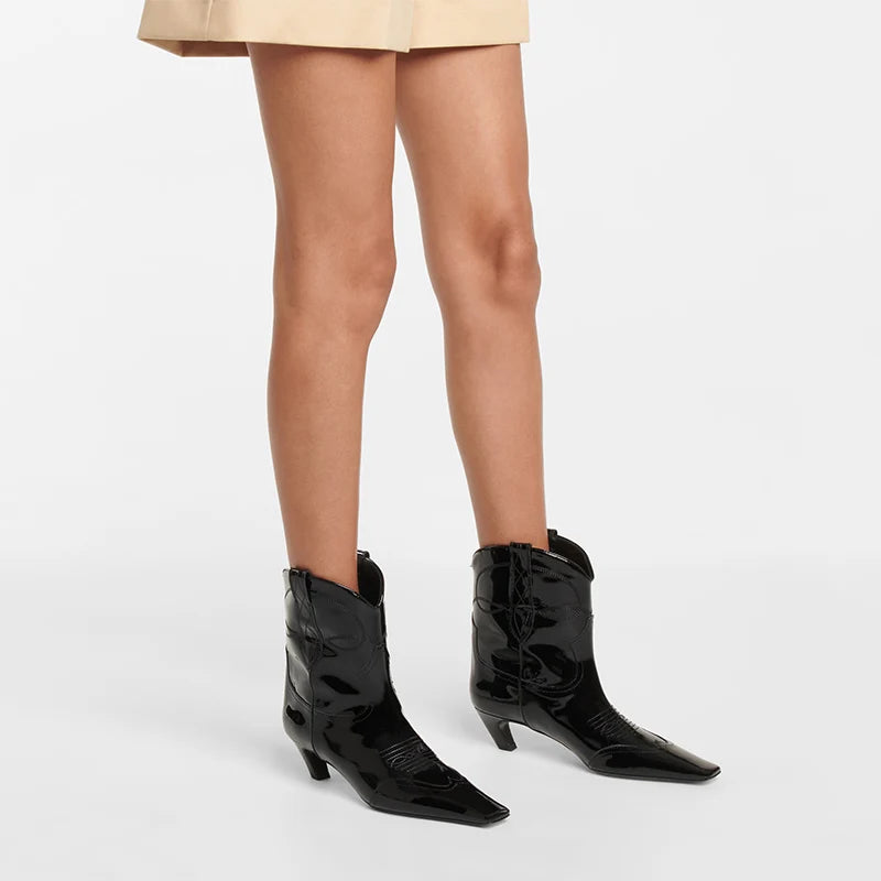Glossy black patent leather Western boots with pointed toes, decorative stitching, and kitten heels.