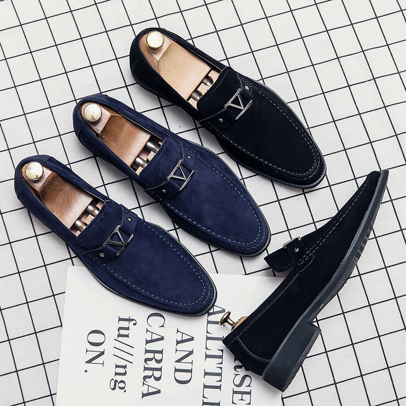 Four black suede loafers with silver metal buckles and wooden shoe trees on a grid background.