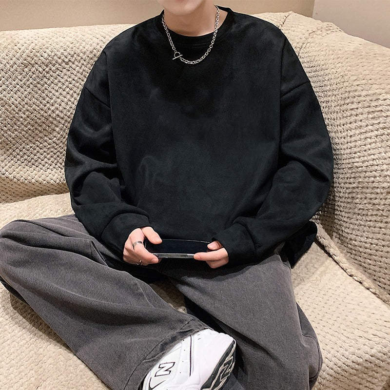 A person wearing a solid black crewneck sweatshirt in a soft velour fabric with an oversized, relaxed style.