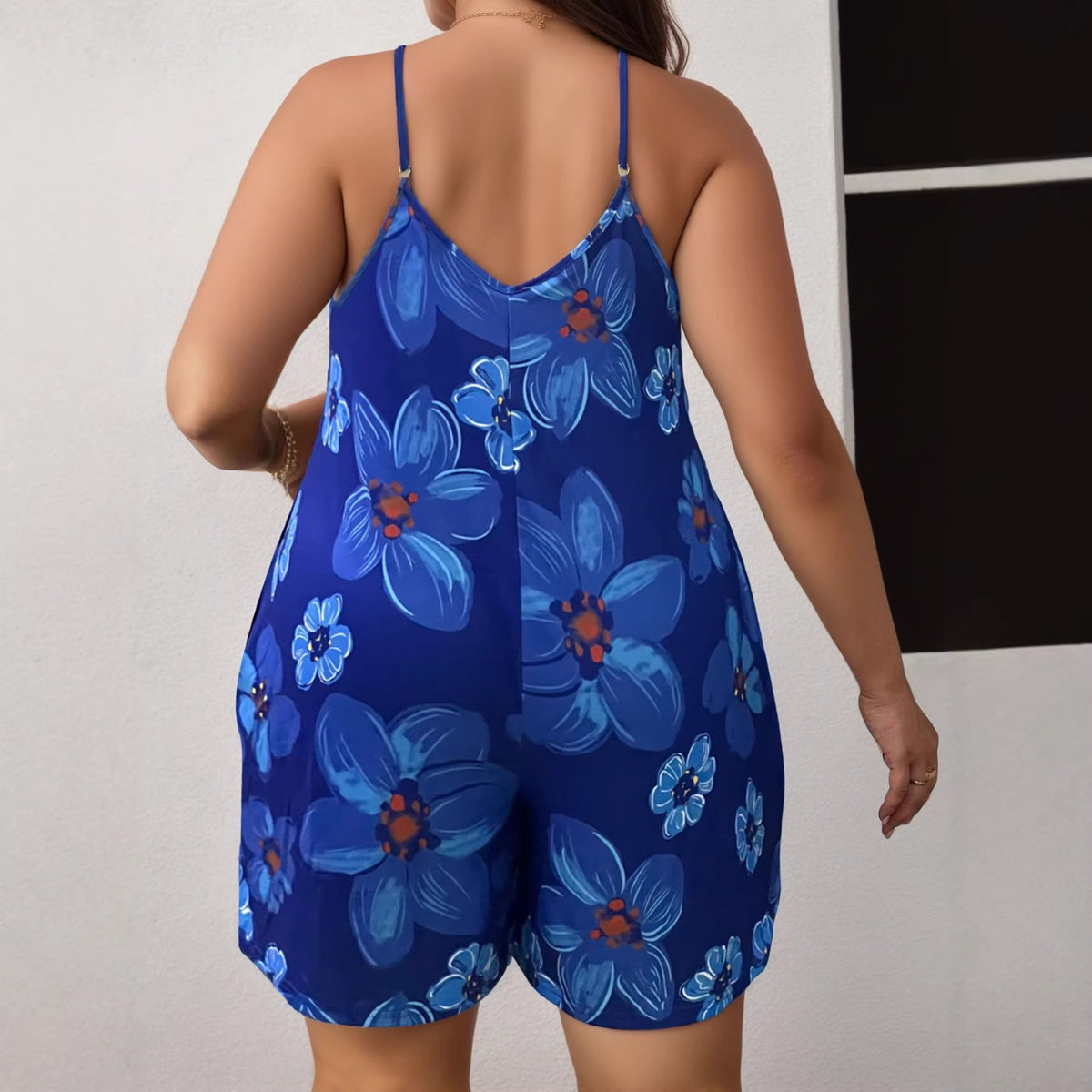 Back view of a blue floral print romper with thin straps worn by a plus-size woman.