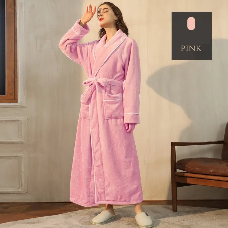 A long pink plush fleece bathrobe with a tie belt, shawl collar, pockets, and white trim, worn by a model.