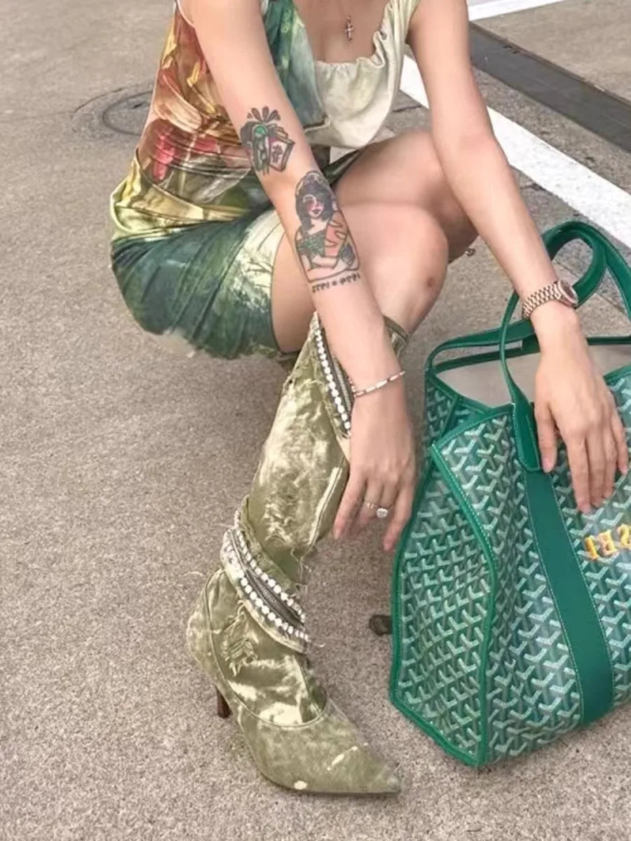 Olive green velvet knee-high boots with beaded strap details, paired with a green patterned tote bag.