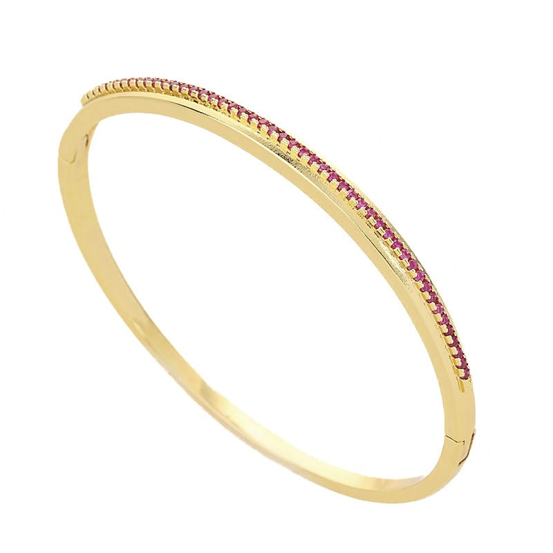 Gold metal bangle bracelet featuring a row of small pink stones along the top edge, with a hinged clasp.