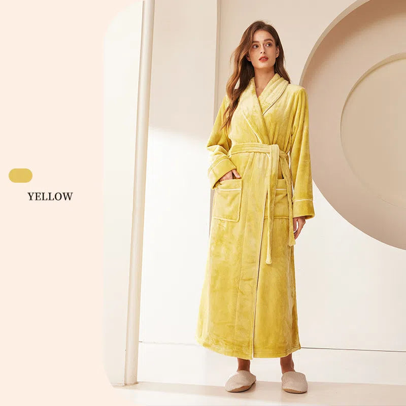 A woman wearing a long, yellow fleece bathrobe featuring a shawl collar, waist tie, and two front pockets.