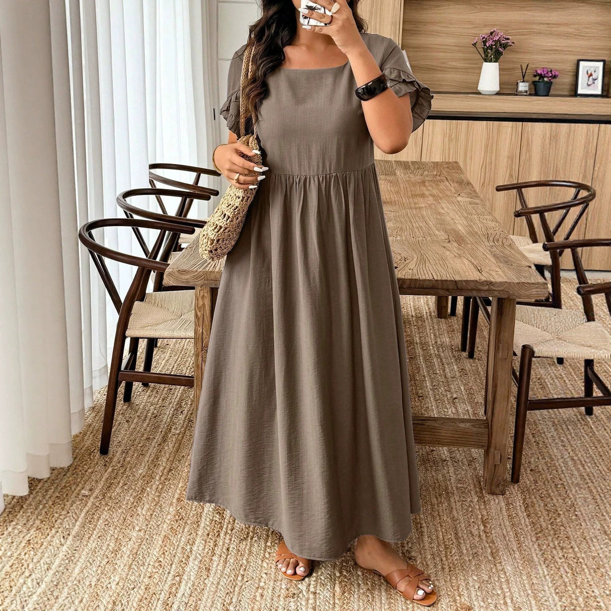 A person in a solid brown cotton midi dress with ruffled sleeves and gathered waist, carrying a straw bag.
