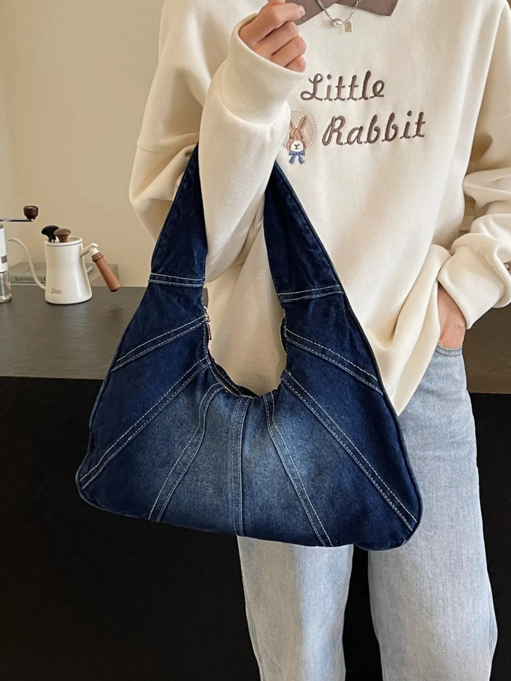 Dark blue denim hobo bag with white topstitching details and a slouchy design held by a person.