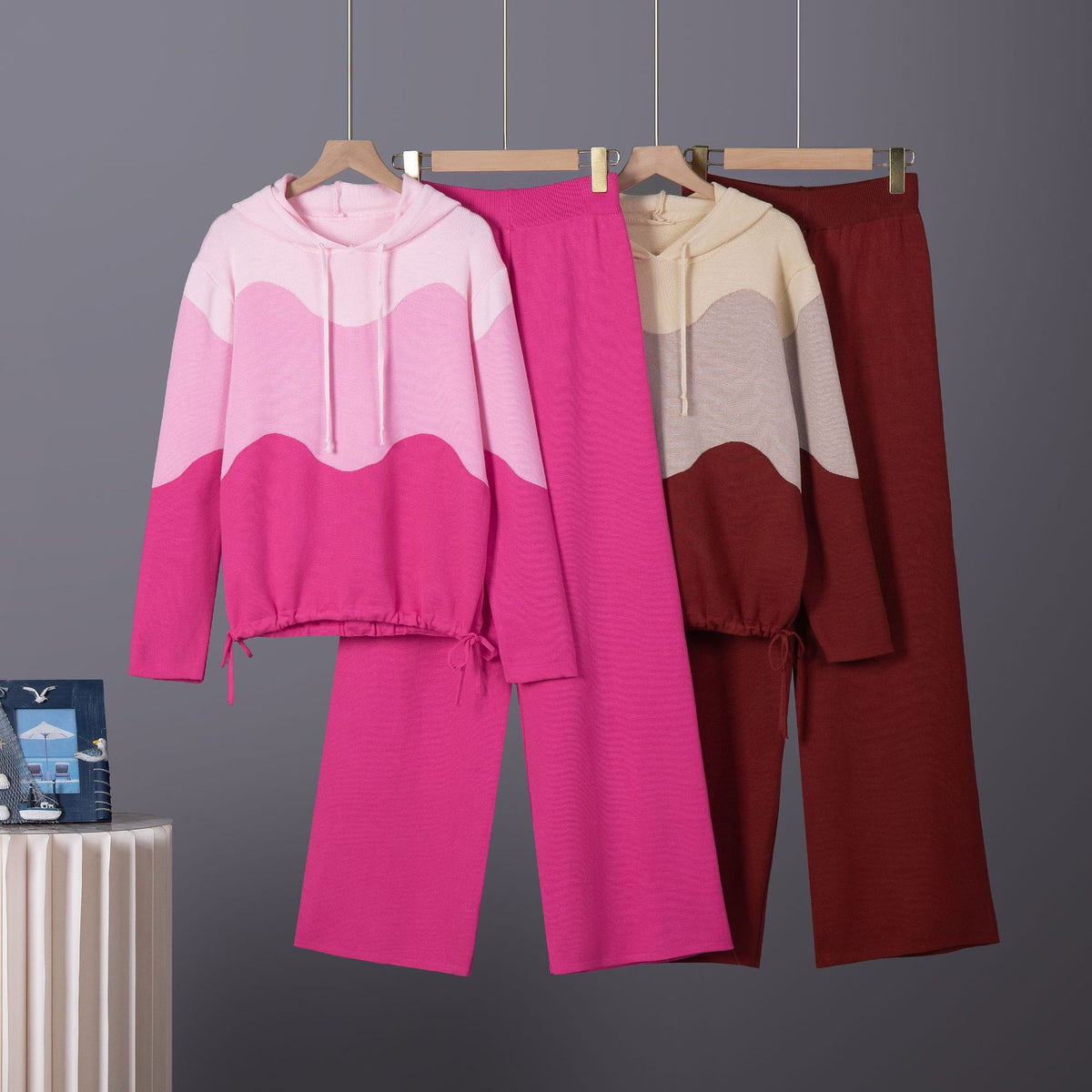 Two knit lounge sets with wavy color-block hoodies and wide-leg pants, one pink and one burgundy.