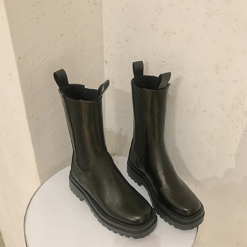 Black Chelsea boots in smooth leather, featuring chunky lug soles, elastic side panels, and front-and-back pull tabs.