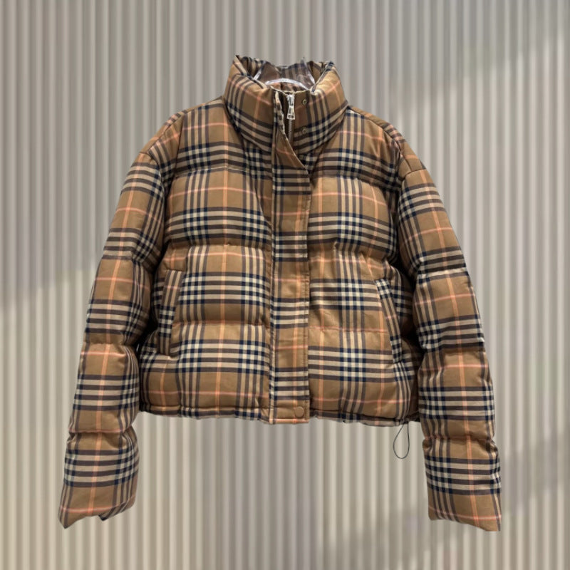 A short beige puffer jacket with a black and orange plaid pattern hangs against a striped wall.