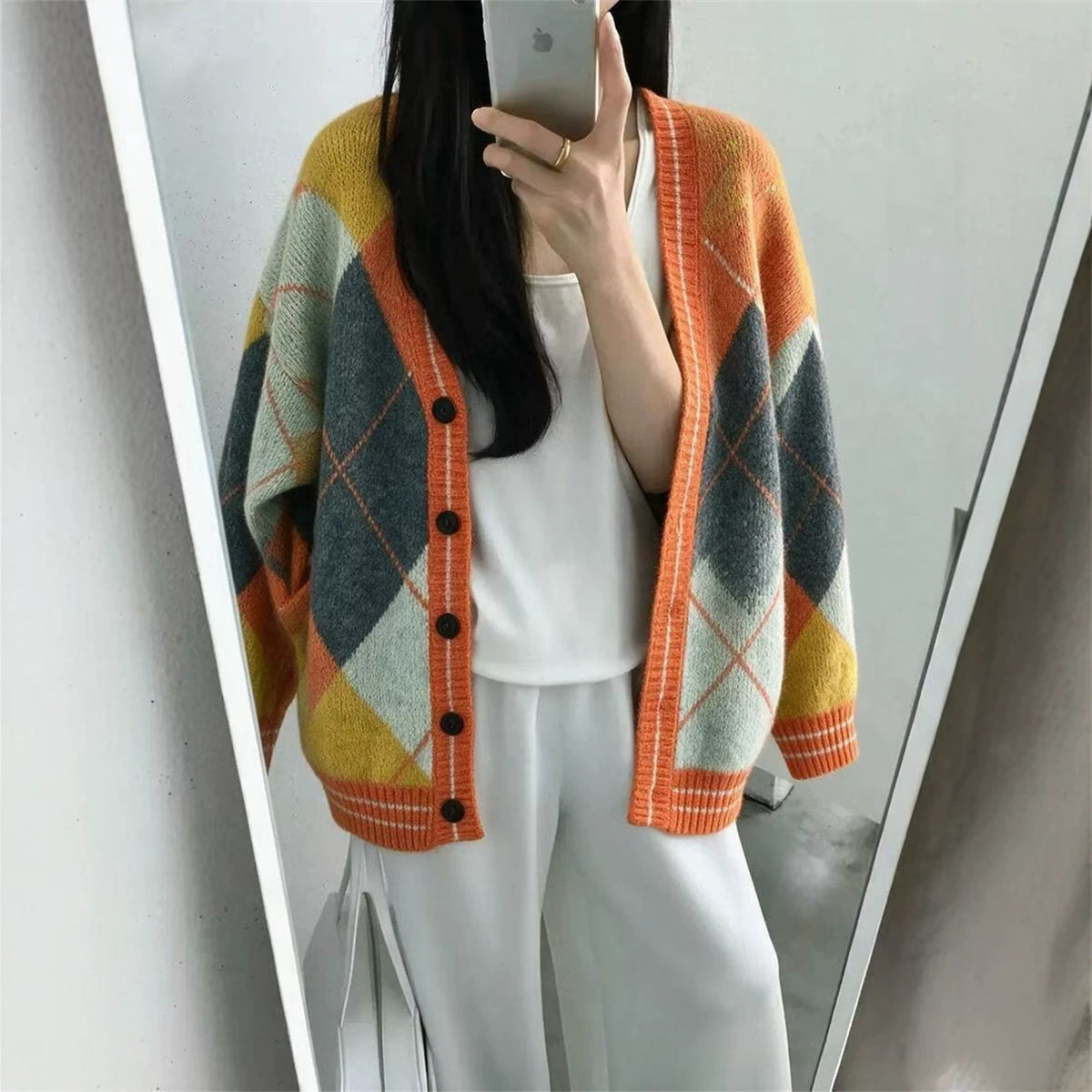 A person wears an oversized, V-neck knit cardigan with a color-blocking diamond argyle pattern in orange, grey, yellow, and white.