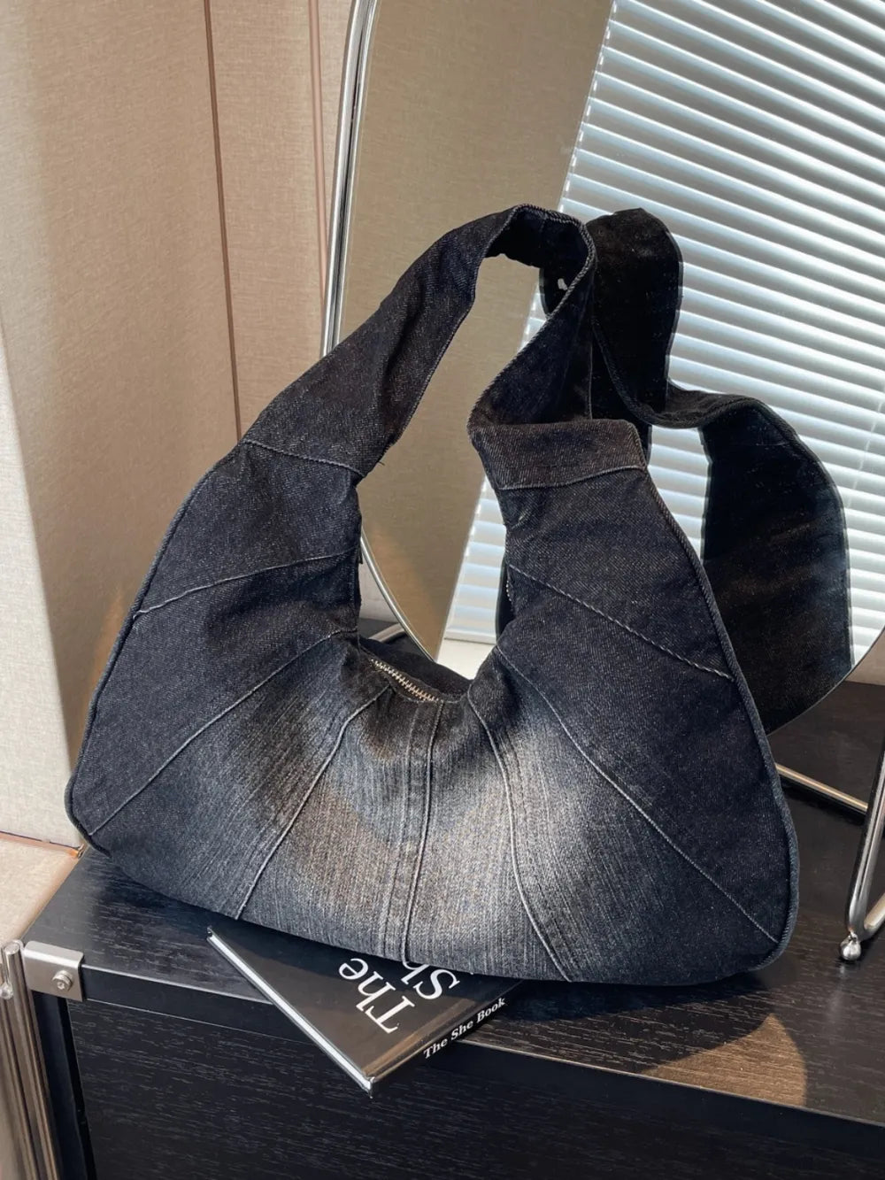 Dark grey denim slouchy hobo bag with a panel design, zipper closure, and thick shoulder strap.