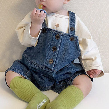 Baby wearing blue denim overalls, white long-sleeve shirt, and green knee-high socks.