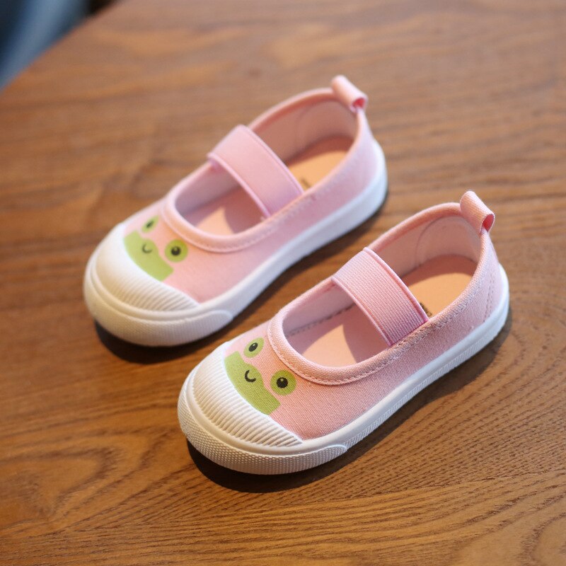 Pink canvas Mary Jane shoes with white rubber soles, elastic straps, and a green frog face on the toe.