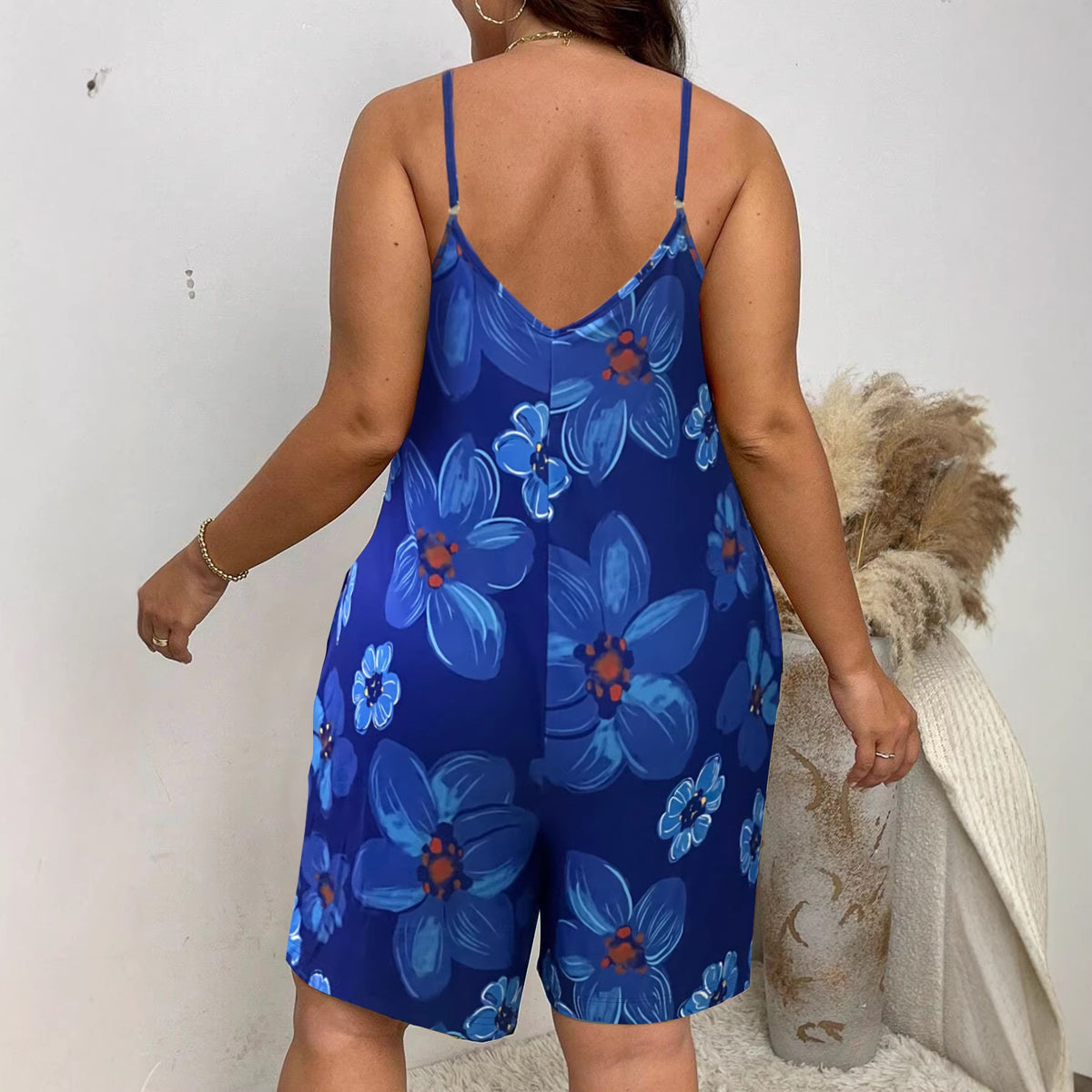 A woman viewed from behind wears a blue sleeveless romper printed with large blue flowers.