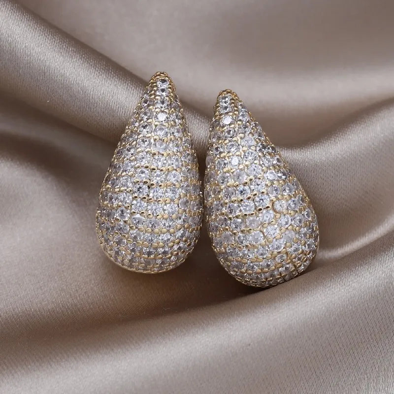 A pair of pavé-set teardrop earrings rests on a draped satin background.