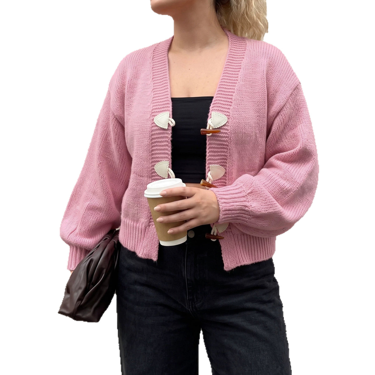 A pink knit cardigan with horn buttons, worn over a black top and jeans.