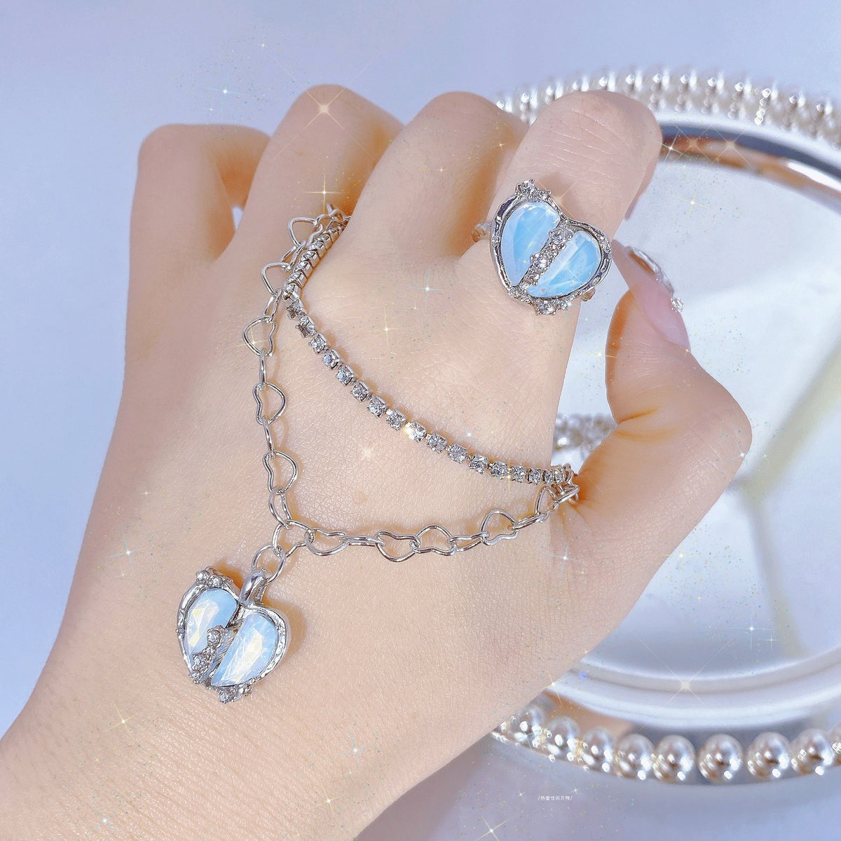 A silver-toned ring and a double-chain bracelet with blue split-heart charms worn on a hand.