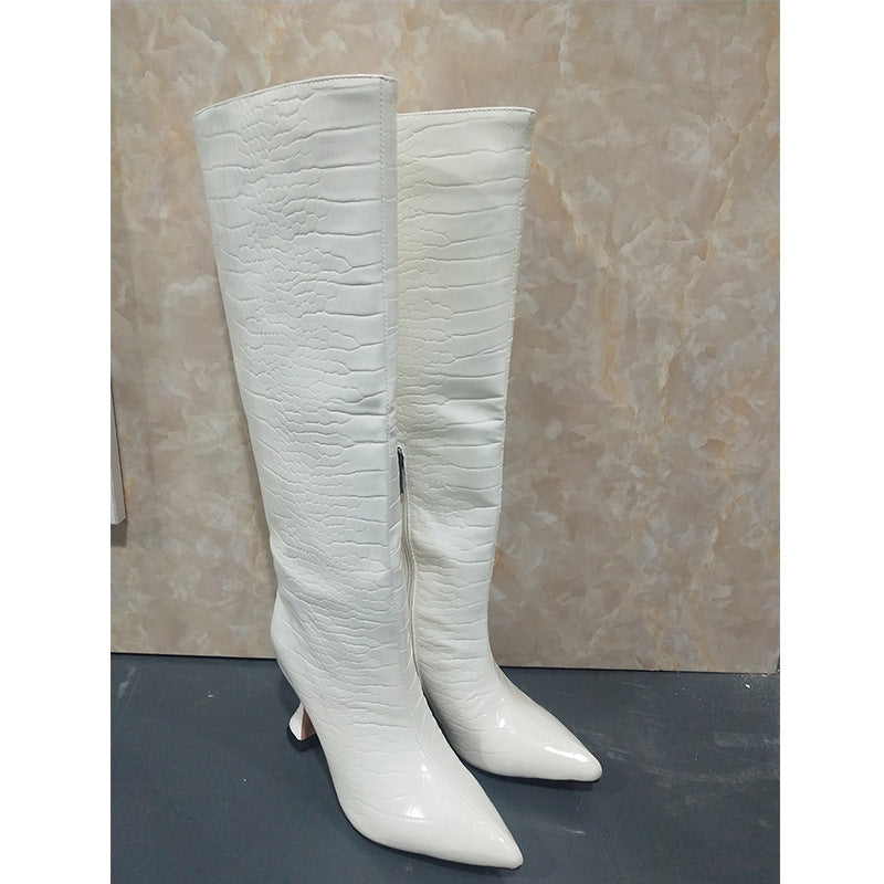 White faux-leather knee-high boots with a glossy finish and a crocodile-skin texture, pointed toes, and flared heels.