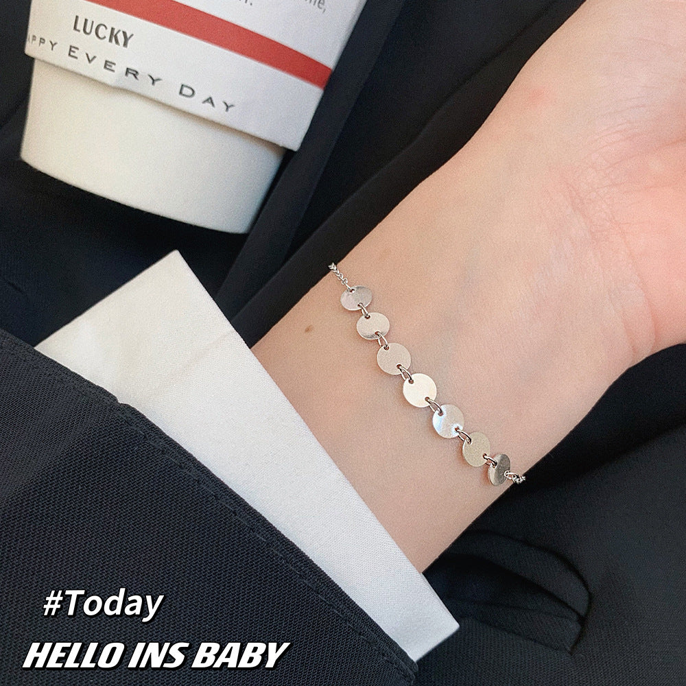 A silver chain bracelet featuring flat round charms worn on a person's wrist.