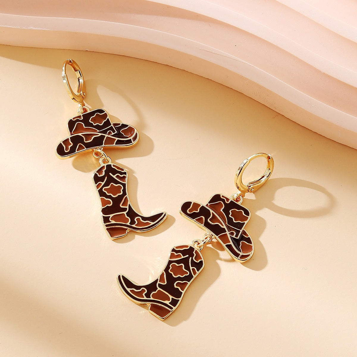 Gold enamel cowboy hat and boot earrings in brown cow print style.