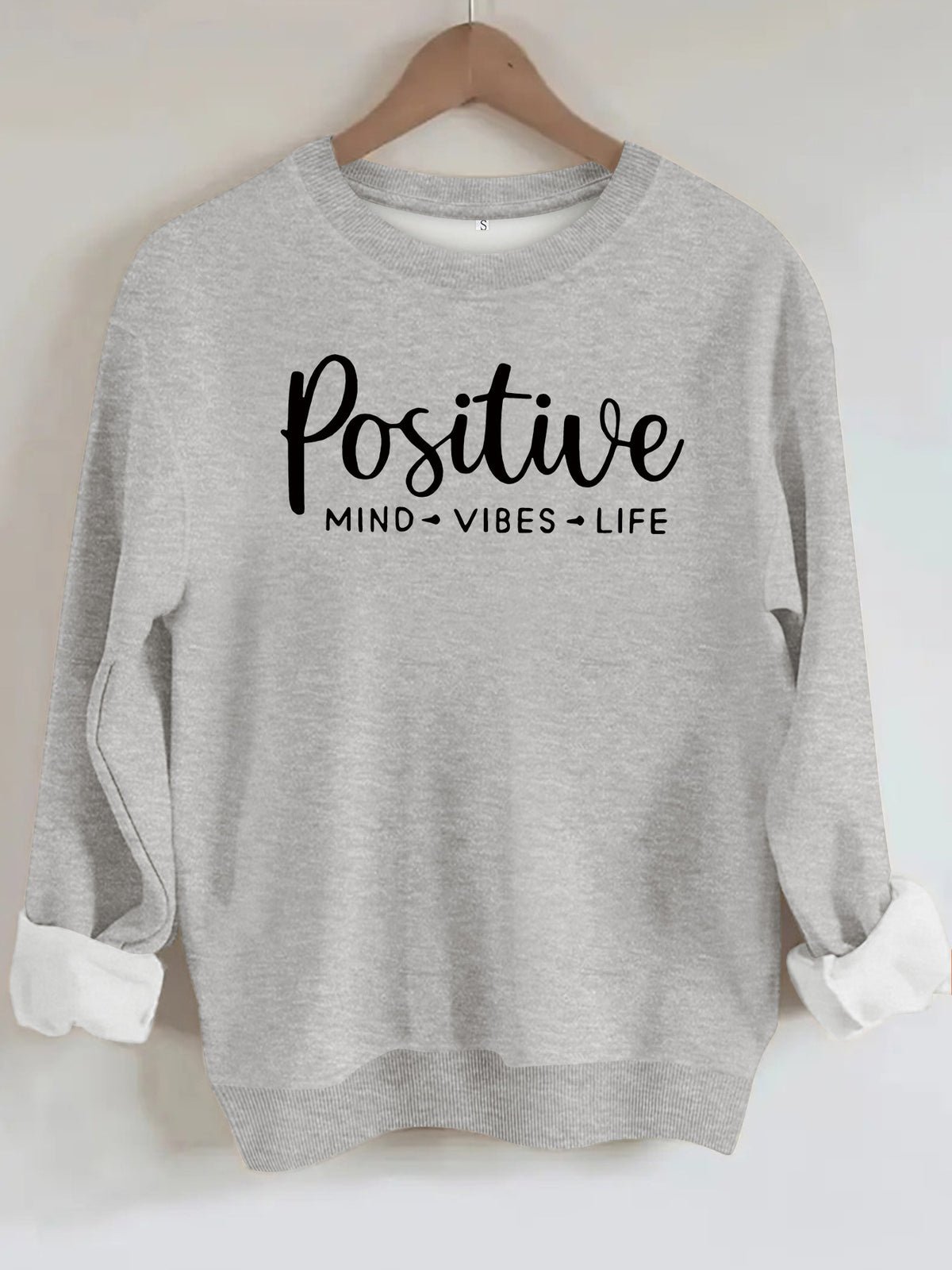 Heather gray crewneck sweatshirt with black "Positive Mind Vibes Life" text graphic on chest, cuffed sleeves.