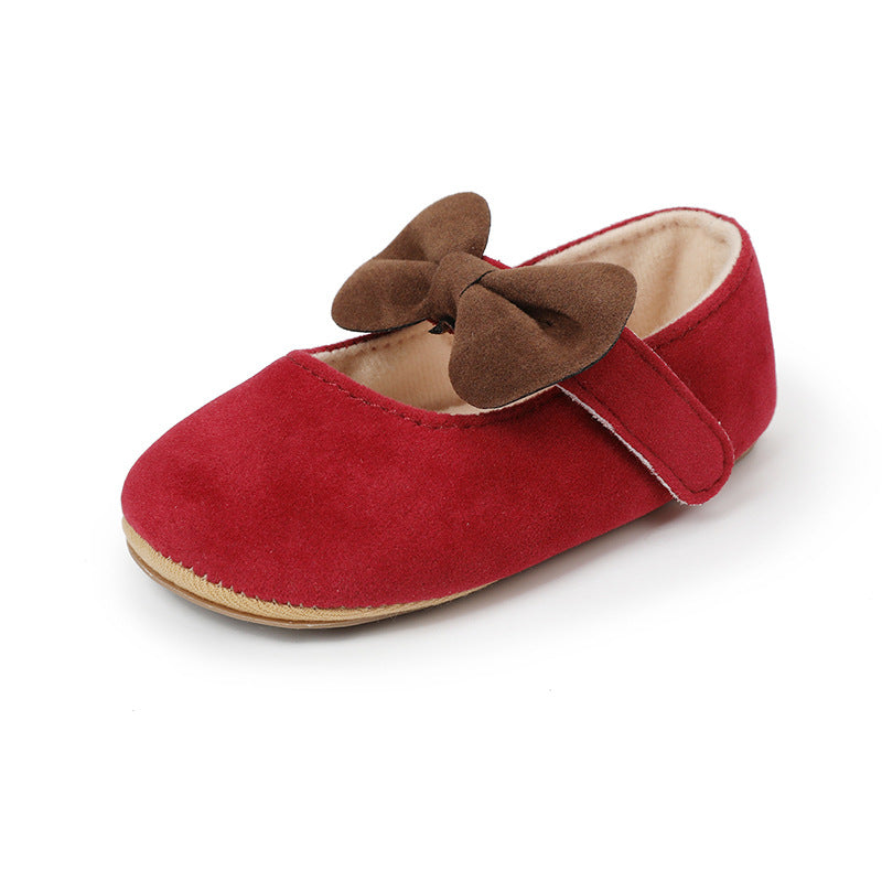 Red suede baby shoe with a brown bow, strap, and beige lining on a white background.