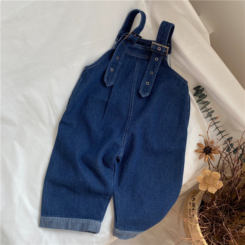 Dark blue denim overalls with cuffed hems, adjustable buckled straps, and decorative front straps with grommets.