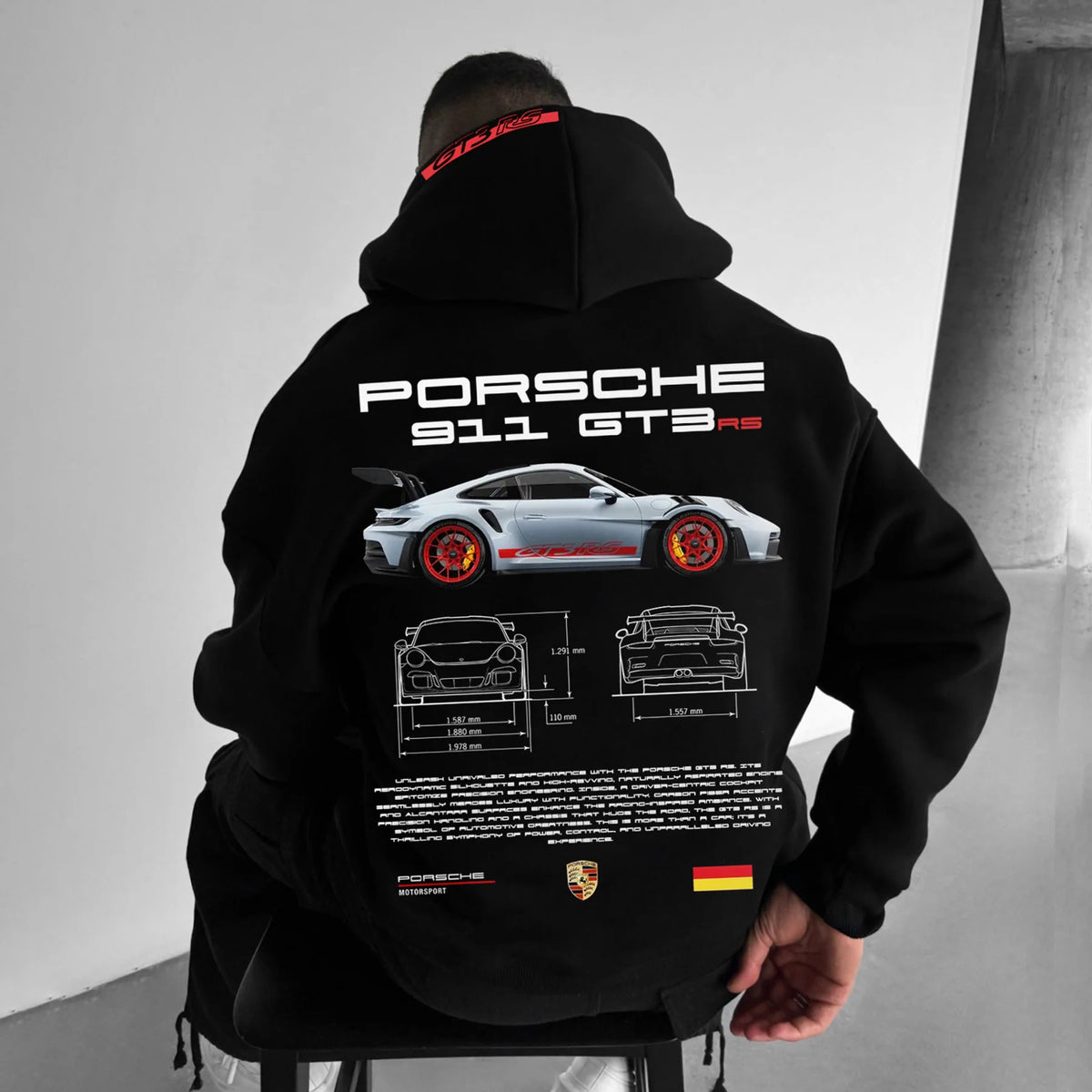 A man wears a black hoodie featuring white and red Porsche 911 GT3 RS car graphics on the back.