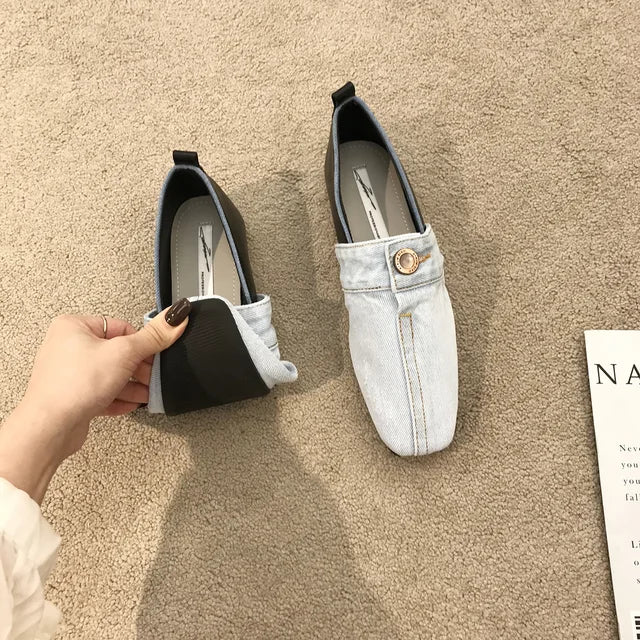Light blue denim slip-on shoes with black trim and a decorative center button, showing a flexible sole.