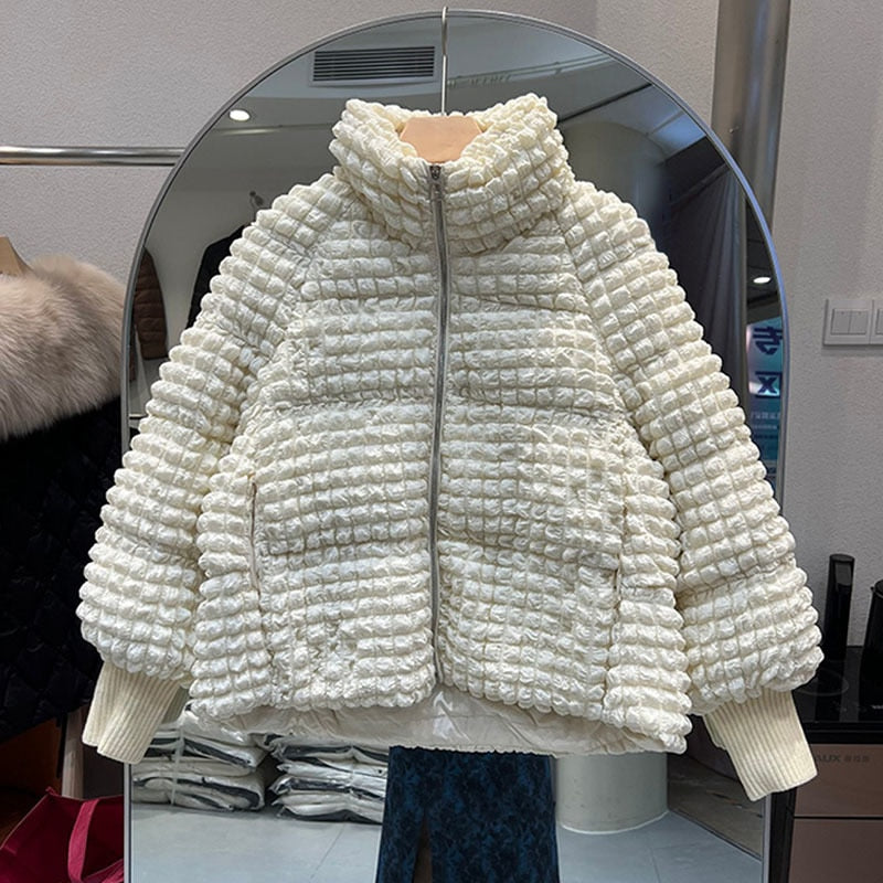 A short, white puffer jacket with a textured, puckered grid pattern and a stand collar hangs against a mirror.