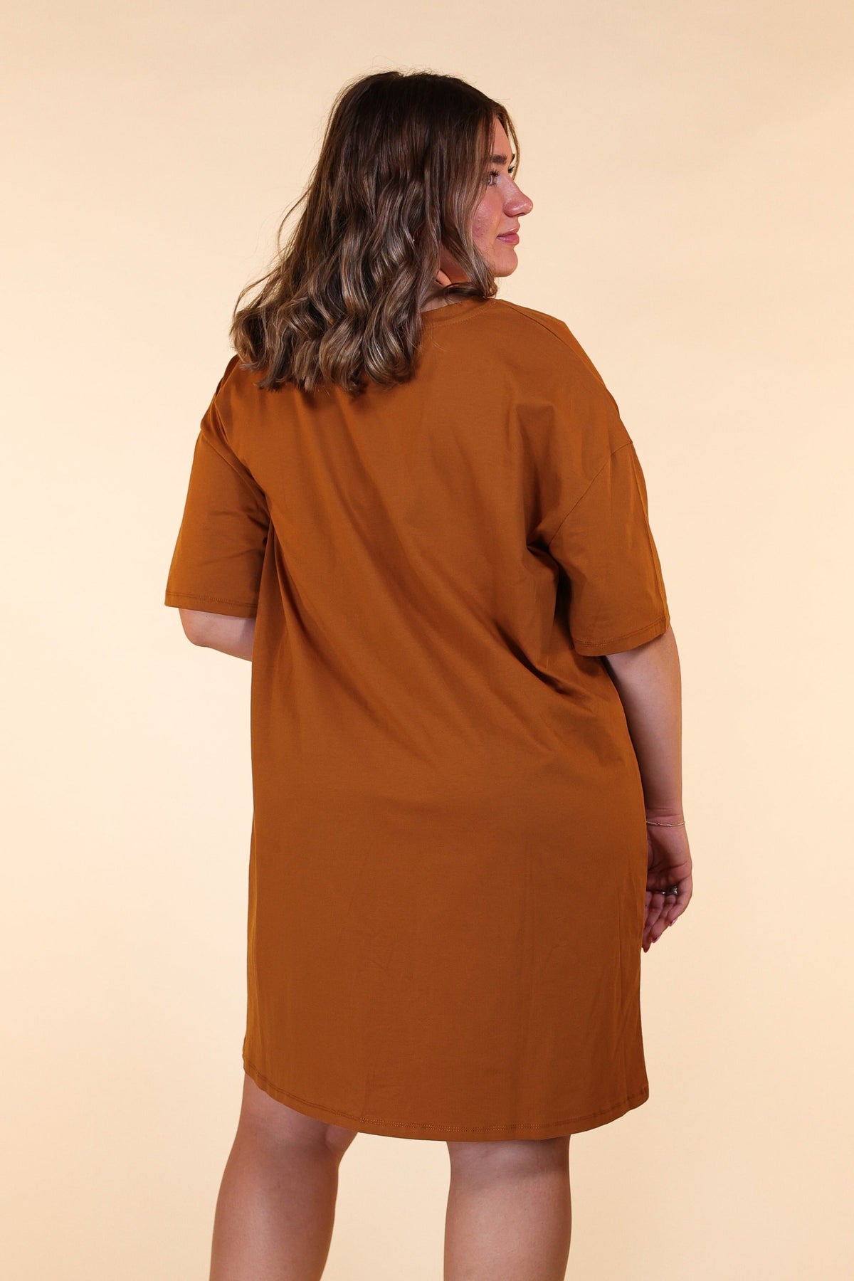 A plus-size woman wearing a rust-colored t-shirt dress, shown from the back against a plain beige background.