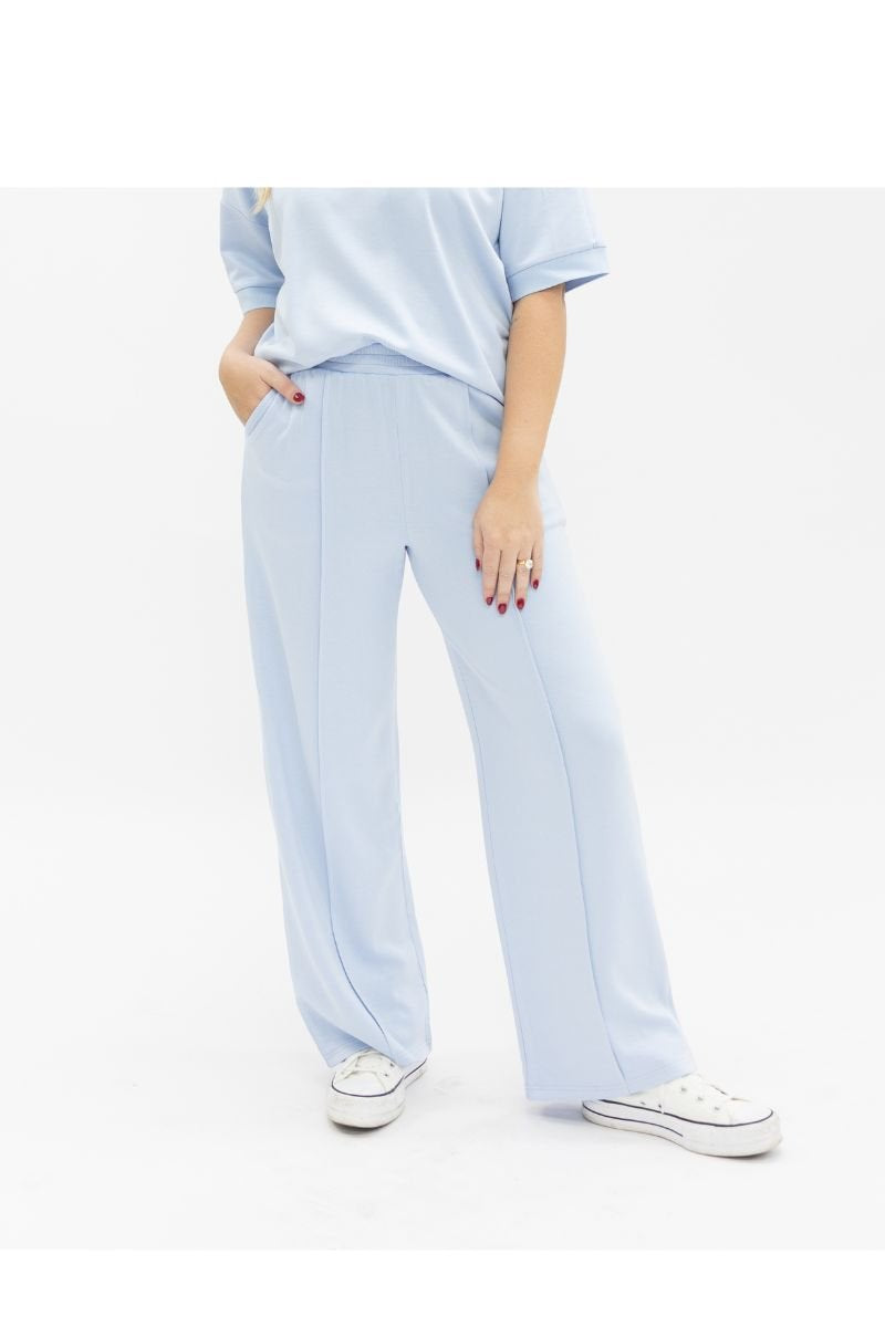 A woman wears light blue, wide-leg ladies pants with a matching short-sleeve top and white sneakers.